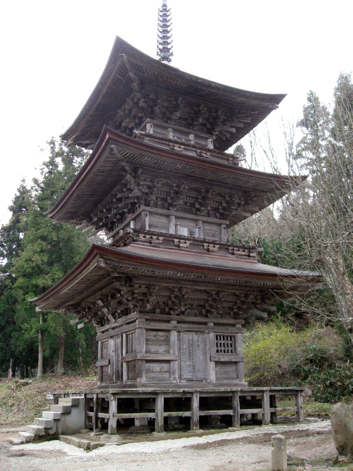 The three-storied wooden pagoda of Hoyoji Temple, raised on a wooden platform, with trees and bare branches around it.