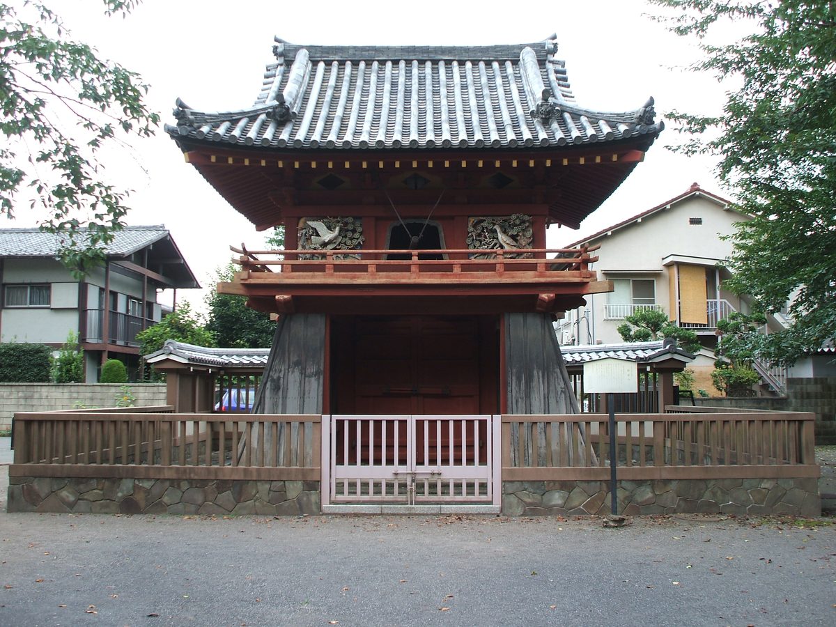 A two-storey red-painted gate with a bell storey above, a curved tiled roof and a low wooden fence in front.