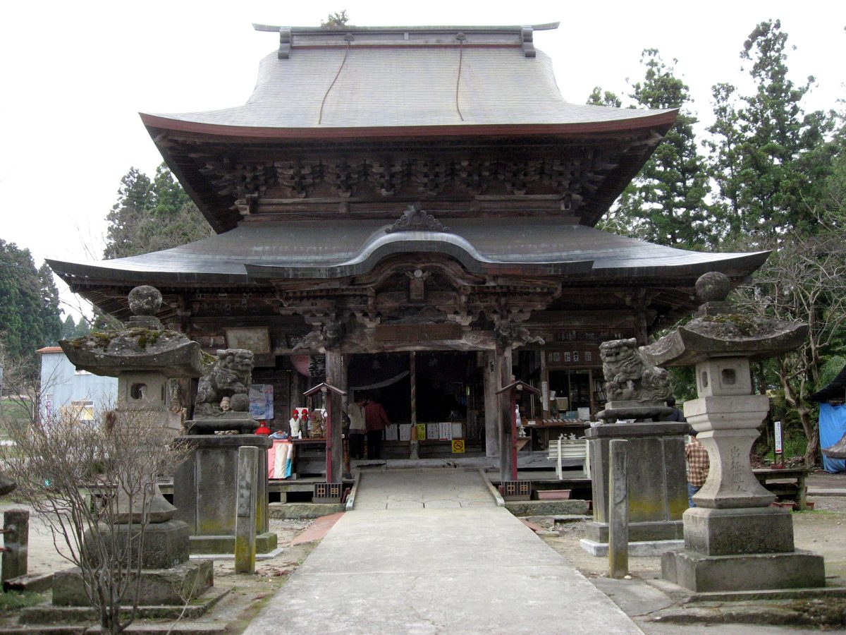 The Kannon hall of Koanji Temple (Nakada Kannon), a wooden hall with a large double roof and carved eaves, approached by a paved path between stone lanterns.