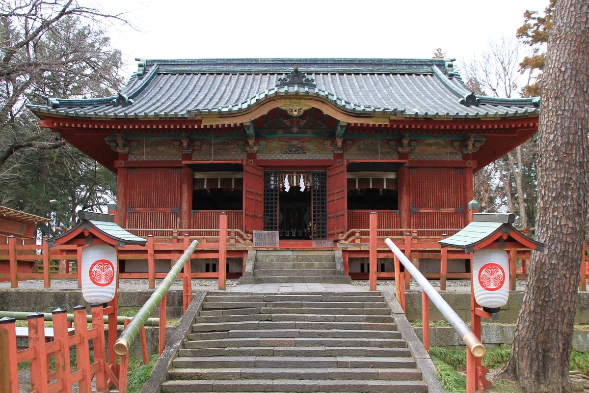 The red worship hall of Serada Toshogu at the top of a flight of stone steps, with a lantern on each side.